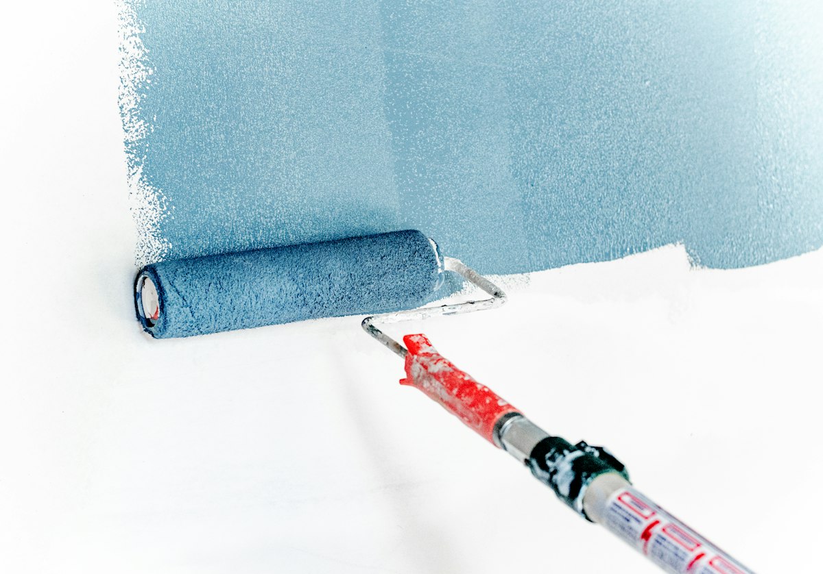 Paint roller laying a fresh blue coat on a white wall